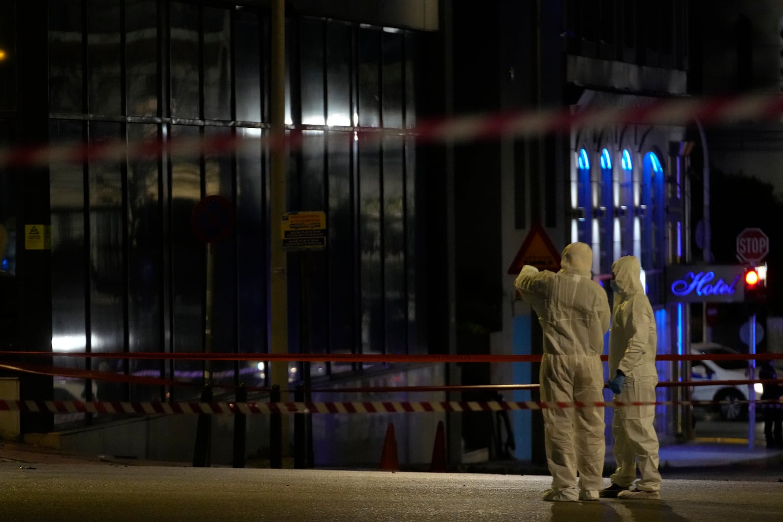 Police investigators wearing coveralls inspect the site after a bomb explosion outside of the Hellenic Train offices the company that runs Greece's railway, the first building on the left, in Athens, Greece, Friday, April 11, 2025. (AP Photo/Petros Giannakouris)