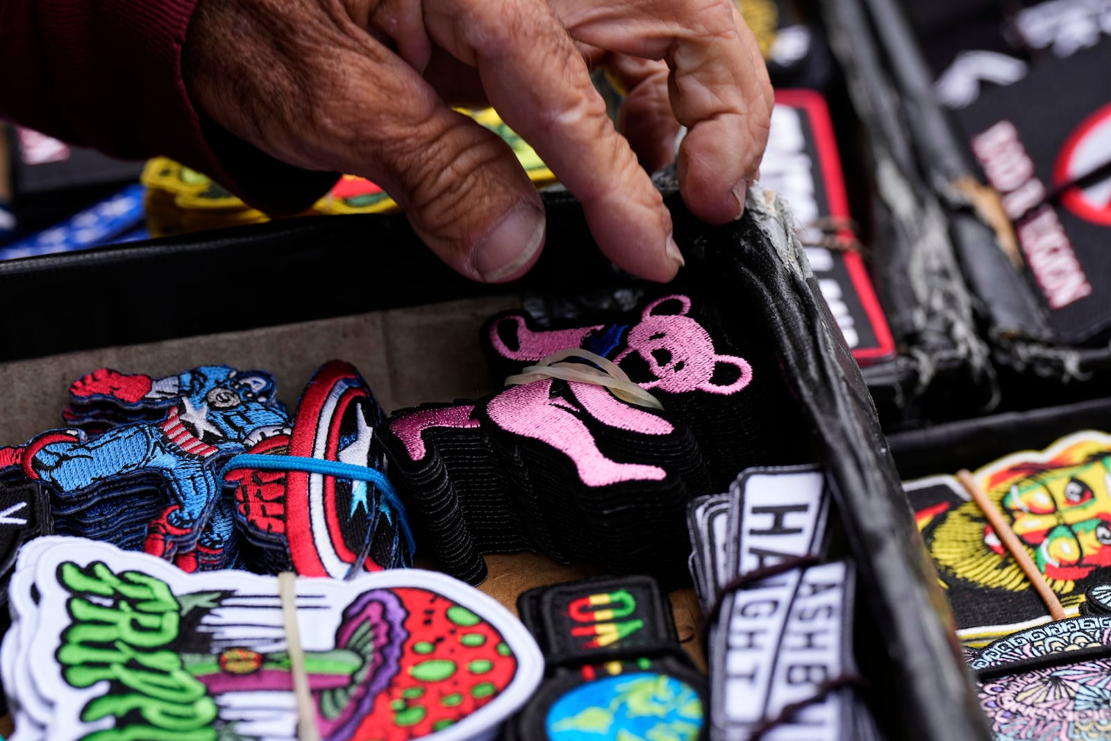 A merchant picks up a Grateful Dead patch out his inventory for a customer in San Francisco, Saturday, July 19, 2025. (AP Photo/Godofredo A. Vásquez)