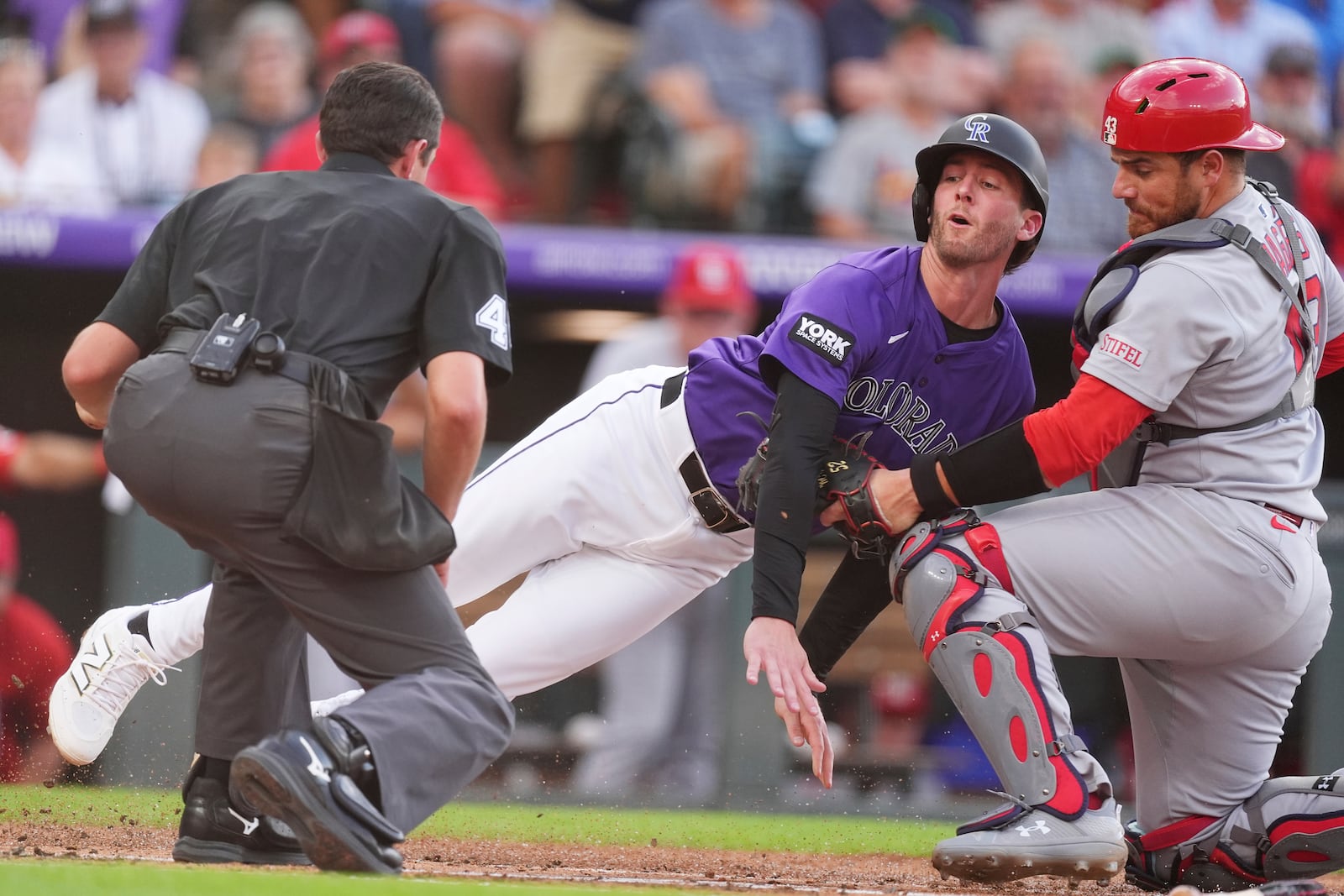 As home plate umpire Willie Trynor, left, waits to make the call as Colorado Rockies' Ryan McMahon, center, is tagged out by St. Louis Cardinals catcher Pedro Pagés, right, while trying to score on a ground ball hit by Rockies' Yanquiel Fernández in the second inning of a baseball game Monday, July 21, 2025, in Denver. (AP Photo/David Zalubowski)