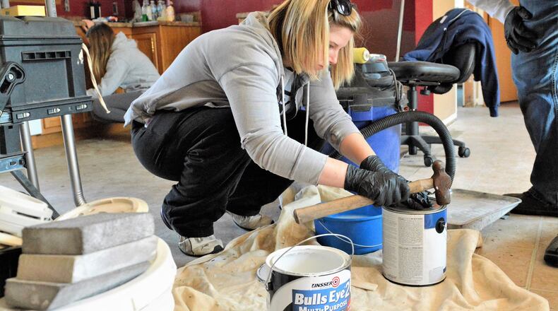 Lindsey Peoples, an employee of Piqua’s Crane Pumps, prepares paint at a Habitat for Humanity house undergoing renovations in Troy. Fellow employee and volunteer Brooke Kiefer works in the background cleaning kitchen cabinets. CONTRIBUTED