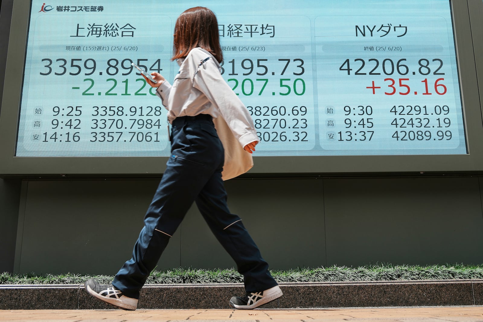 A person walks in front of an electronic stock board showing Shanghai, Japan's Nikkei and NY Dow indexes at a securities firm Monday, June 23, 2025, in Tokyo. (AP Photo/Eugene Hoshiko)