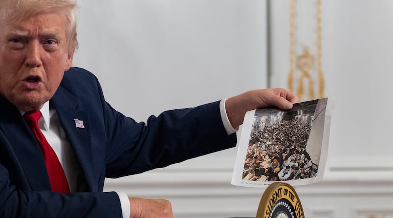 President Donald Trump holds up a photograph as he speaks to reporters after speaking to troops via video from his Mar-a-Lago estate on Thanksgiving, Thursday, Nov. 27, 2025, in Palm Beach, Fla. (AP Photo/Alex Brandon)