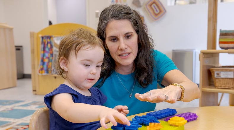 Nicole Myrick, director of Mini University at Sinclair Community College, explains a toy to a child on Tuesday, March 10. Childcare providers in Ohio have always had small profit margins, but new regulations have increased both the amount of hours required to hit reimbursement and the amount of money reimbursed, challenging some childcare providers. BRYANT BILLING / STAFF