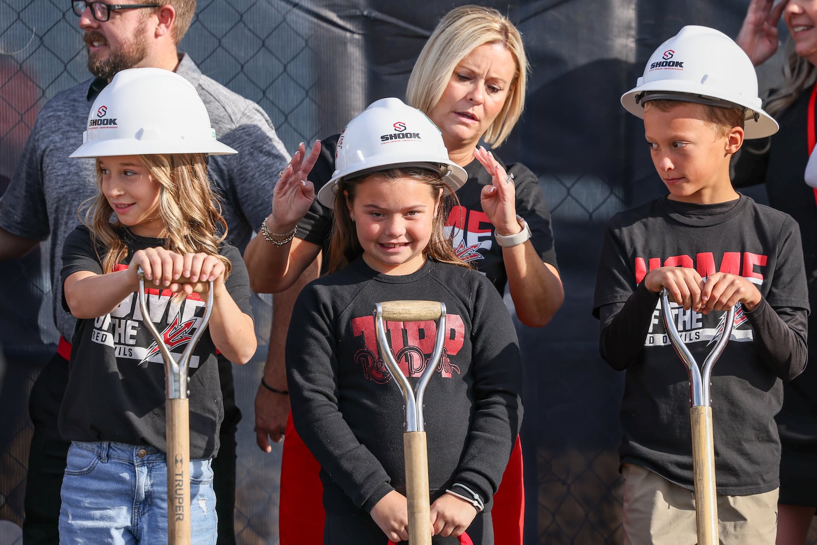 LT Ball Intermediate School principal Kari Hake adjusts the helmet she put on third grader Addy Chaney's head during a groundbreaking celebration Tipp City Schools held Friday, Oct. 17 for its new prekindergarten through eighth grade school, which is being constructed on North Hyatt Street on land between the existing Tippecanoe Middle School and Ball Intermediate. BRYANT BILLING / STAFF