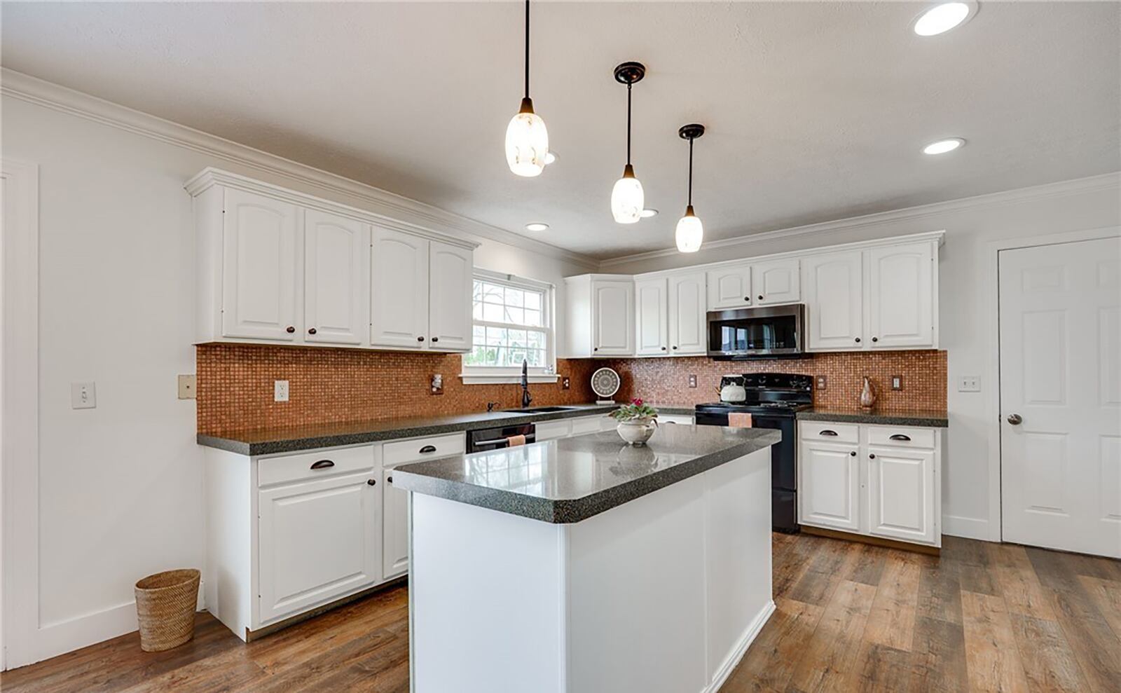 The kitchen has an island, eat in breakfast area, granite countertops and white cabinets.