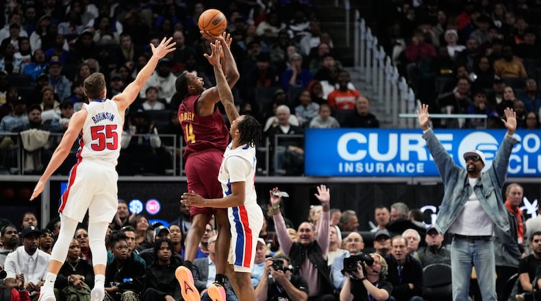 Cleveland Cavaliers center Evan Mobley, center, shoots against Detroit Pistons forward Duncan Robinson, left, and guard Ron Holland II, third from left, as former NBA player Jalen Rose, right, reacts during the first half of an NBA basketball game, Monday, Oct. 27, 2025, in Detroit. (AP Photo/Ryan Sun)