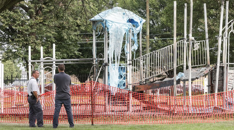 A Dayton police officer and a city maintenance worker talk on Monday, Aug. 4, 2025, at Bomberger Park while looking over playground equipment that was destroyed in a fire early Sunday morning. BRYANT BILLING / STAFF