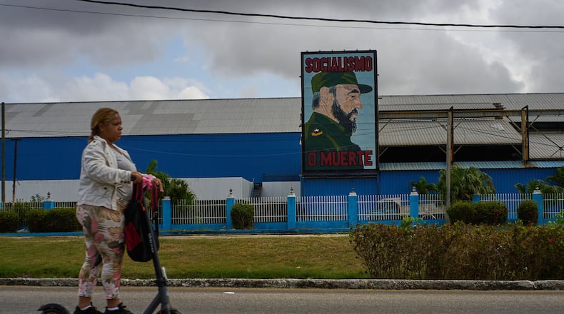 A woman rides an electric scooter past a factory displaying an image depicting the late Cuban leader Fidel Castro, bearing the words "Socialism or Death", in Havana, Cuba, Thursday, March 19, 2026. (AP Photo/Ramon Espinosa)