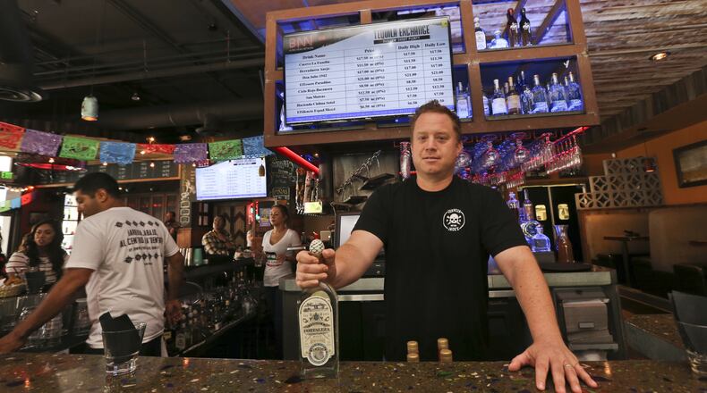 Frank Miller, a partner in a series of eight bars in San Diego, shows off some of the tequila collection at The Blind Burro, in San Diego, where the tequila prices can change every five minutes based on demand. The electronic Tequila Exchange board, behind and above Miller, shows the current prices for the bar’s tequilas. (AP Photo/Lenny Ignelzi)