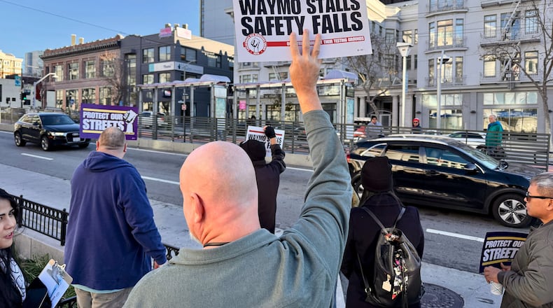 Demonstrators holds signs during a protest by Uber and Lyft drivers asking state regulators to take self-driving taxis off the streets due to safety concerns at the California Public Utilities Commission headquarters Friday, Jan. 9, 2026, in San Francisco. (AP Photo/Haven Daley)