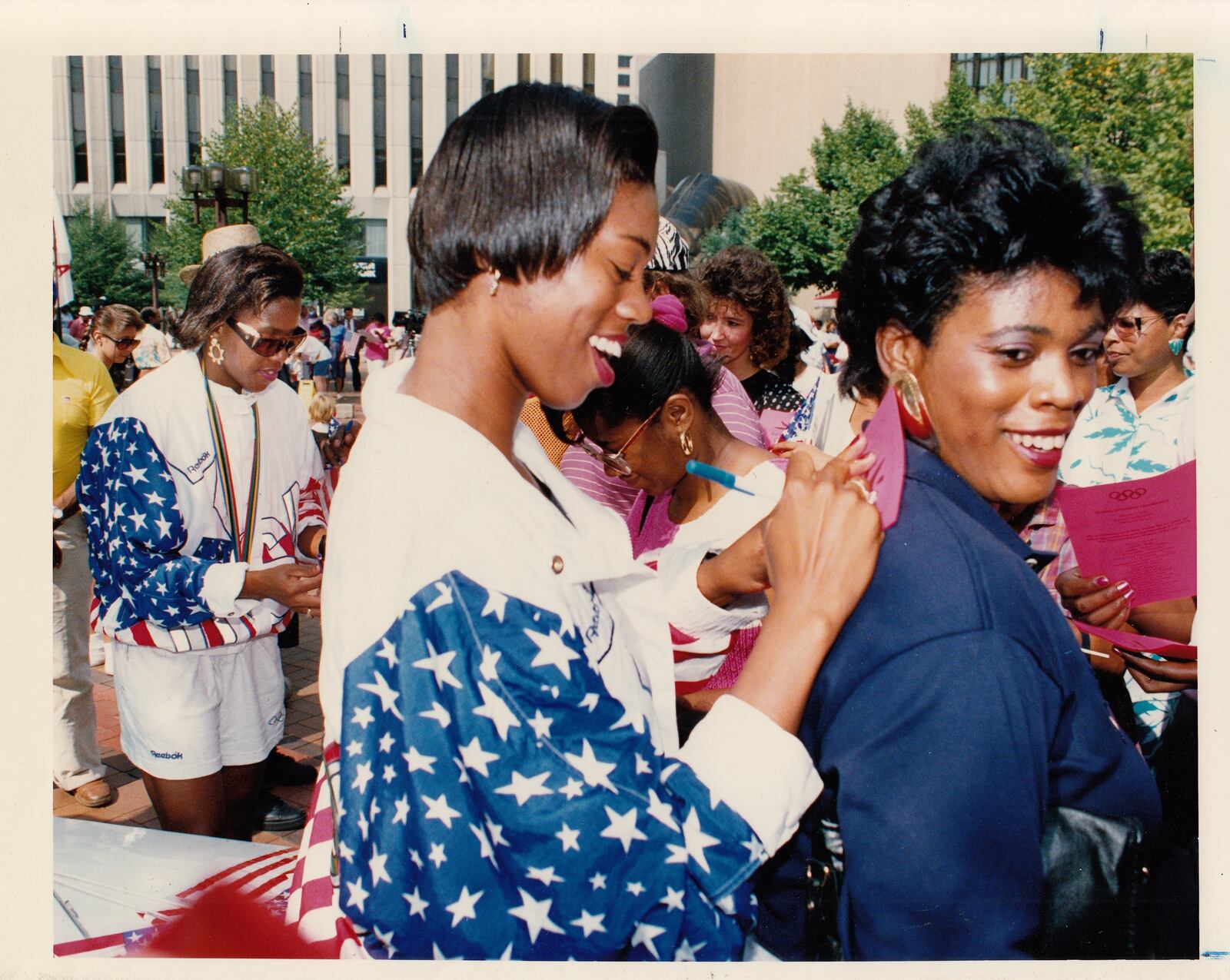 Tonja Buford (center) uses her mother Georgianna's back as support as she and Lavonna Martin (behind left) sign autographs at Courthouse Square following the Olympic Parade in August, 1992. DDN STAFF FILE