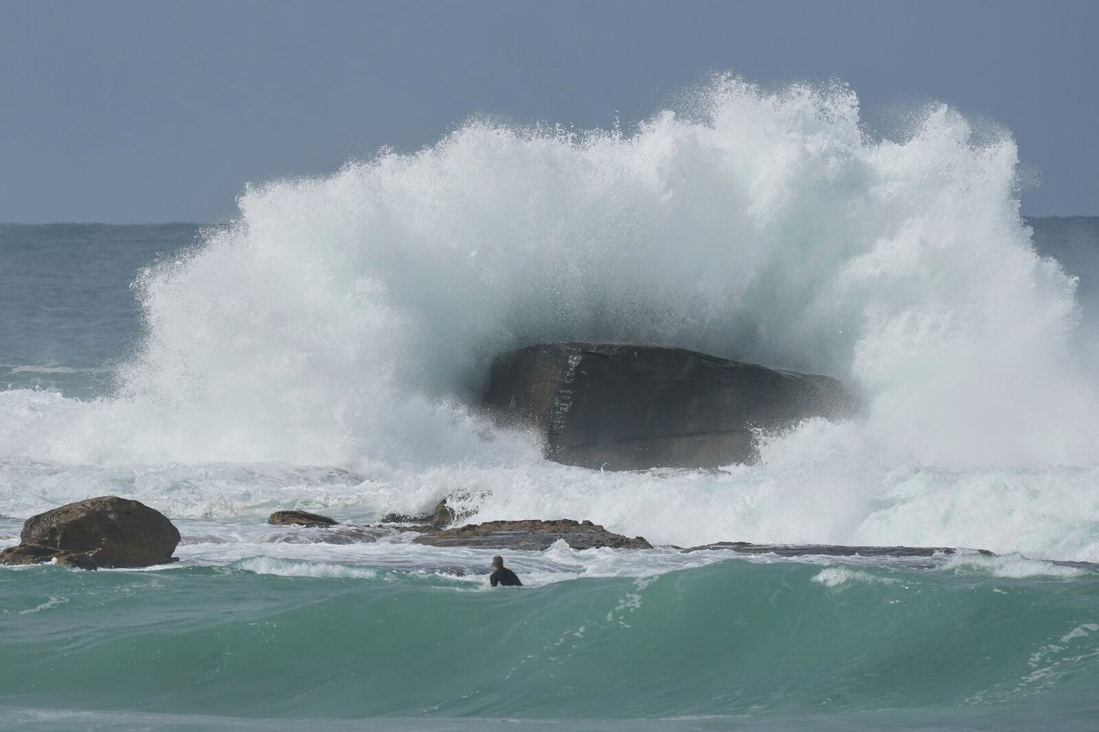 A surfer watches as a large wave hits a rock as large swells hit Sydney's Bondi Beach Wednesday, April 2, 2025. (AP Photo/Mark Baker)