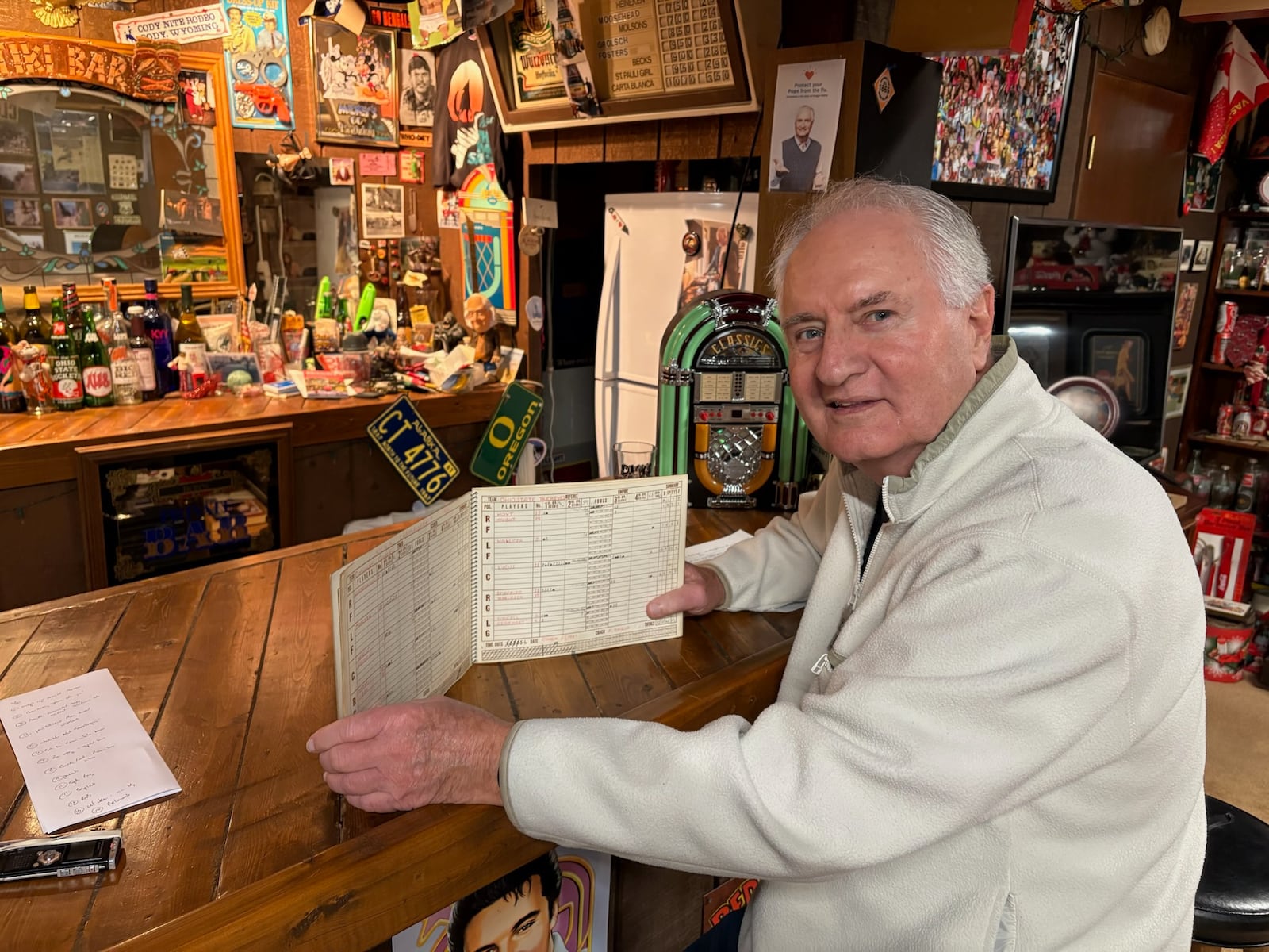 Miamisburg High School boys basketball scorekeeper Ron Anslinger sits at his Elvis Bar in his home earlier this month. Anslinger, a member of the Vikings Miami Valley League championship squad in 1964, has kept the scorebook for the Miamisburg boys basketball program for more than 55 years. TOM ARCHDEACON / CONTRIBUTED PHOTO