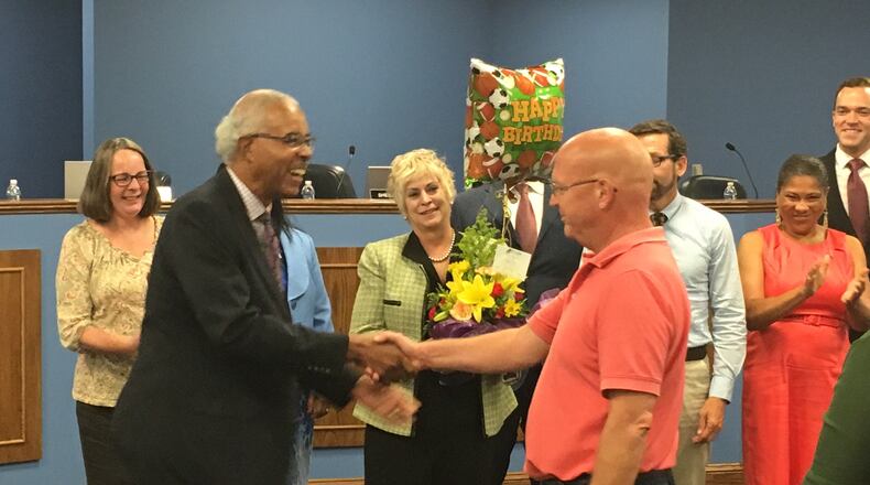 Dayton school board President Robert Walker (left) greets teachers union President David Romick on Tuesday night, as Superintendent Rhonda Corr holds a birthday gift for Romick. JEREMY P. KELLEY / STAFF
