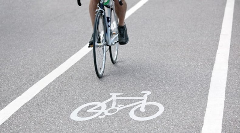 Commuter riding a bicycle on a city cycle lane or path across white painted bike symbol
