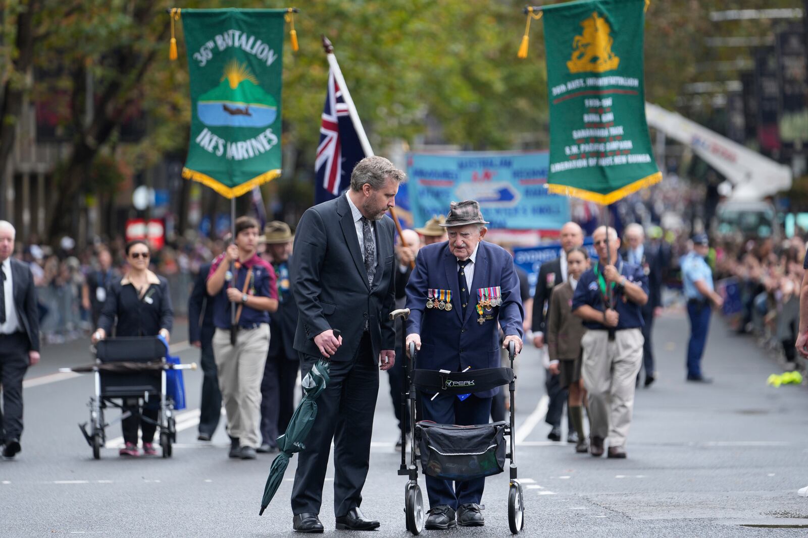A participant is assisted as they march past thousands of people lining the street to pay tribute to their war dead during the Anzac Day parade in Sydney, Australia, Friday, April 25, 2025. (AP Photo/Rick Rycroft)