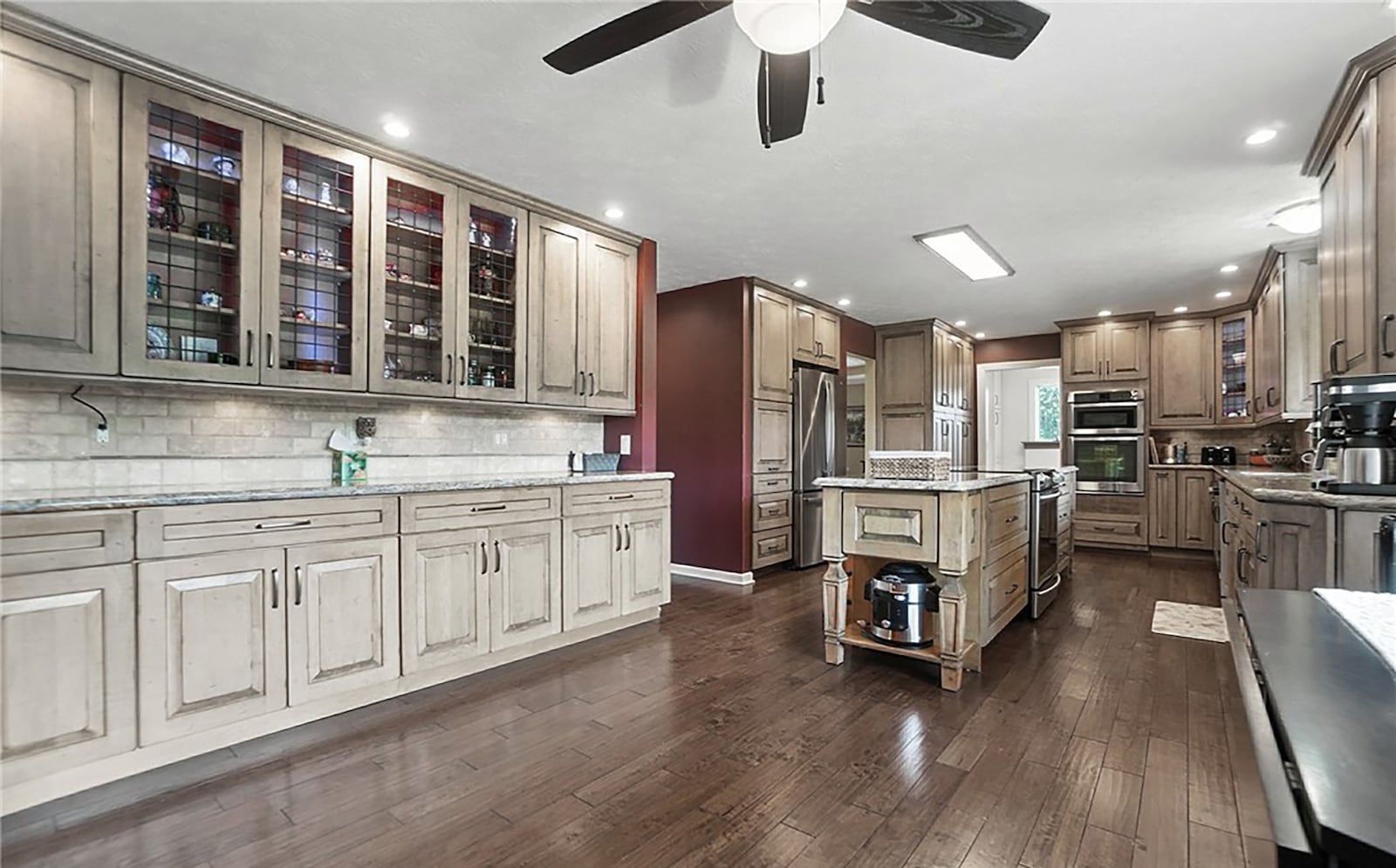 The eat in kitchen has hardwood flooring, custom wood cabinets with an island, quartz countertops and a tile backsplash and a ceiling fan. CONTRIBUTED