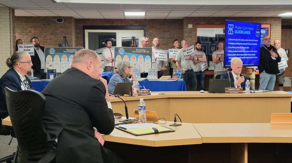 The Xenia Board of Education listens to residents speak at the podium during their regular meeting Monday. Behind them, attendees hold signs that say "We support Xenia employees," October 13, 2025. LONDON BISHOP/STAFF
