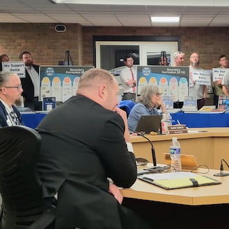 The Xenia Board of Education listens to residents speak at the podium during their regular meeting Monday. Behind them, attendees hold signs that say "We support Xenia employees," October 13, 2025. LONDON BISHOP/STAFF