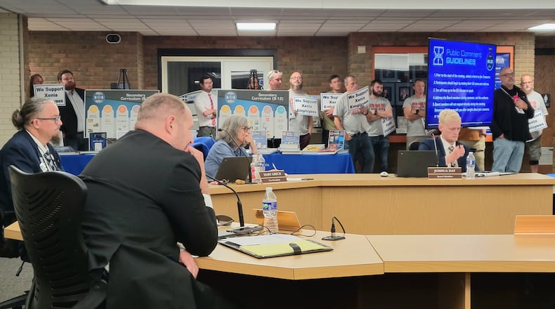 The Xenia Board of Education listens to residents speak at the podium during their regular meeting Monday. Behind them, attendees hold signs that say "We support Xenia employees," October 13, 2025. LONDON BISHOP/STAFF