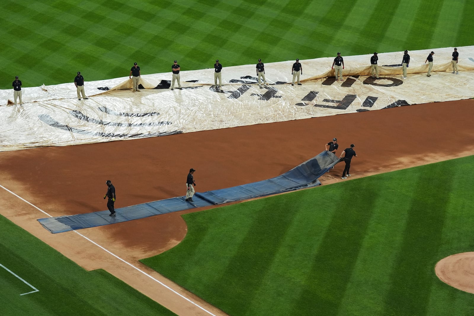 The grounds crew covers the field with a tarp during a rain delay before a baseball game between the Cleveland Guardians and the Chicago White Sox in Chicago, Thursday, July 10, 2025. (AP Photo/Nam Y. Huh)