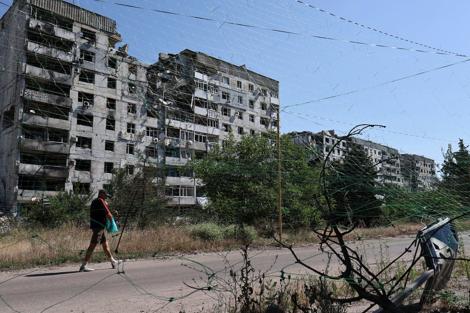 In this photo provided by Ukraine's 65th Mechanized Brigade press service, a local resident walks along the street under an anti-drone net in Orikhiv, Zaporizhzhia region, Ukraine, Tuesday, July 15, 2025. (Andriy Andriyenko/Ukraine's 65th Mechanized Brigade via AP)