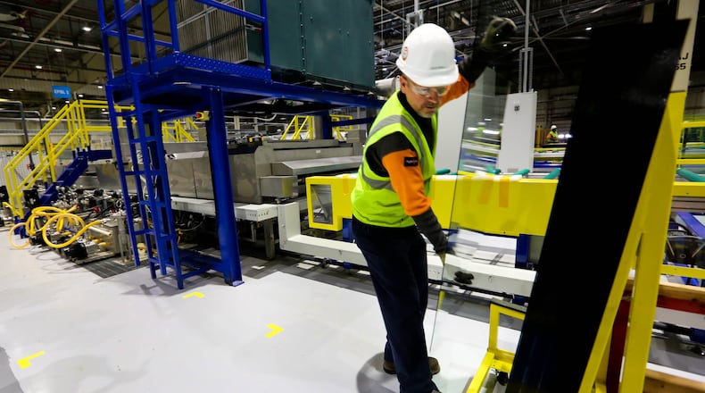 David Wigle takes glass off a Fuyao Glass America production line for sampling in this 2015 photo. Someone who says she is a former Fuyao employee is suing for what she claims is unpaid overtime and wages. JIM WITMER/STAFF