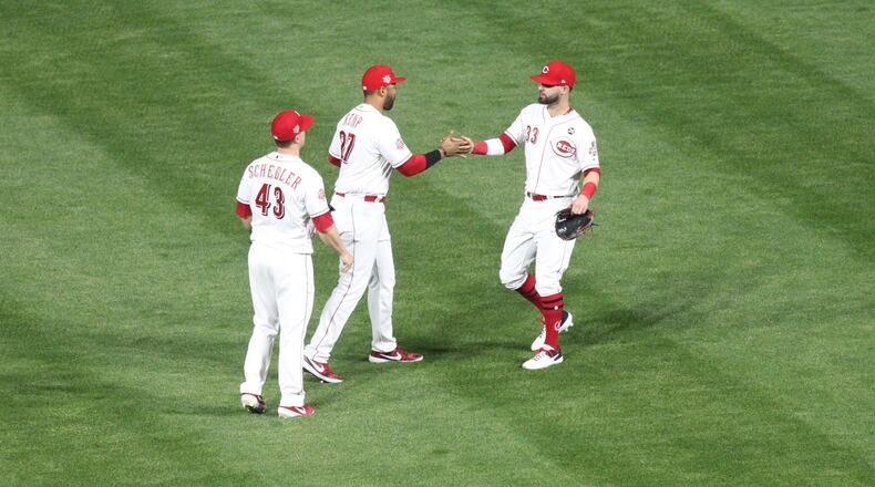 Reds outfielders Jesse Winker, right, and Matt Kemp, center, slap hands as Scott Schebler watches after a victory against the Marlins on Tuesday, April 9, 2019, at Great American Ball Park in Cincinnati. David Jablonski/Staff