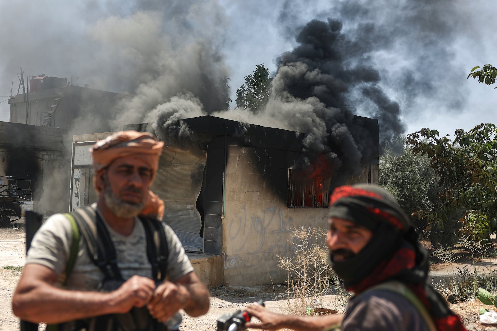 Bedouin fighters stand in front a burned shop at Mazraa village on the outskirts of Sweida city, during clashes between the Bedouin clans and Druze militias, southern Syria, Friday, July 18, 2025. (AP Photo/Ghaith Alsayed)