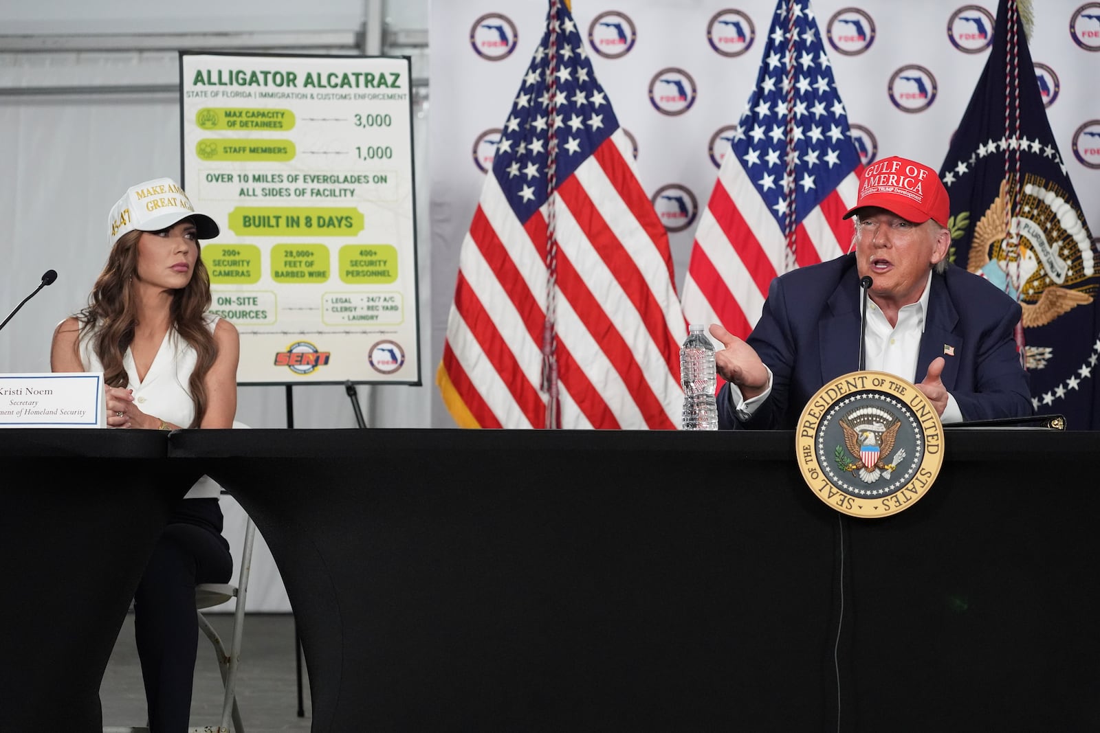 President Donald Trump speaks during a roundtable at "Alligator Alcatraz," a new migrant detention facility at Dade-Collier Training and Transition facility, Tuesday, July 1, 2025, in Ochopee, Fla., as Homeland Security Secretary Kristi Noem, looks on. (AP Photo/Evan Vucci)