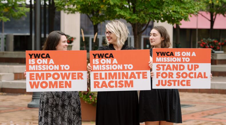 Women from YWCA hold signs explaining the organization's mission since its founding in 1870. The YWCA has acquired UpDayton, which will assist them in achieving this mission.