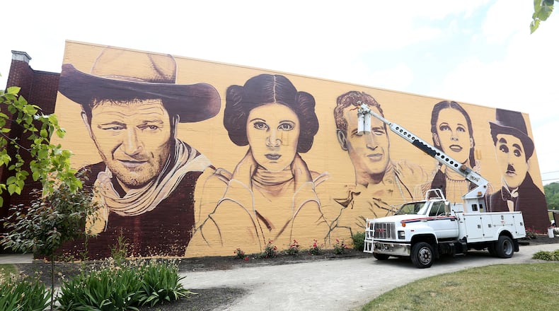 A new mural in downtown Miamisburg pays  tribute to Hollywood legends. Towering portraits - 35- feet tall - of John Wayne, Carrie Fisher, Paul Newman, Judy Garland and Charlie Chaplain have been created on the north wall of the Plaza Theatre, 33 S. Main St. Artist Erica Arndts, a Centerville native, said she wanted to âpay honor to vintage Hollywood characters,â as she put the finishing touches on the 100-foot-long mural. LISA POWELL / STAFF