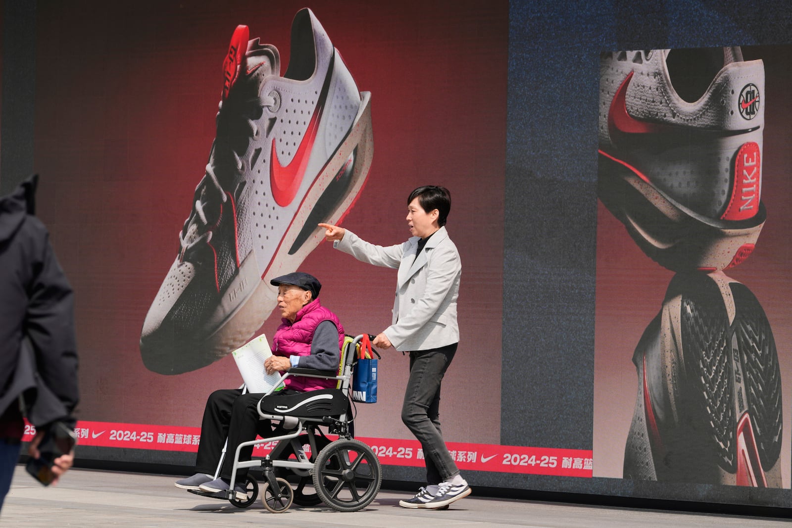 A woman pushes an elderly man past a Nike store at a mall in Beijing, Wednesday, May 7, 2025. (AP Photo/Ng Han Guan)