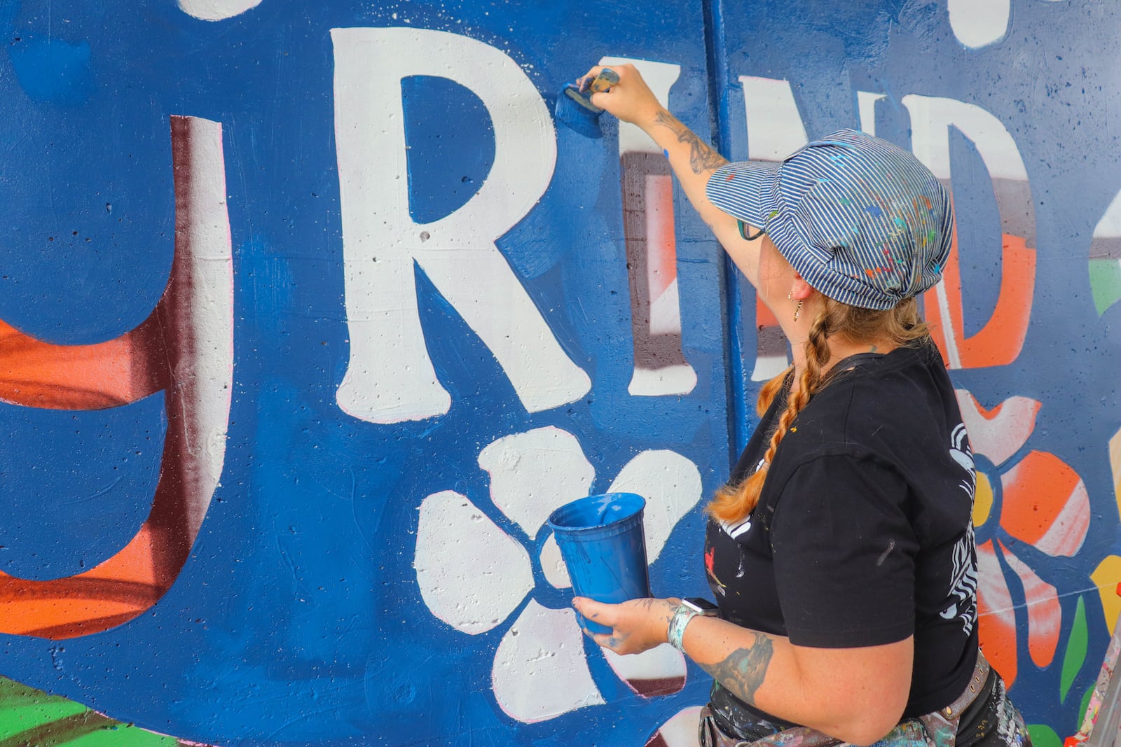 Tiffany Clark repainting parts of her "Don't Let The Bastards Grind You Down" mural on the corner of Keowee and Third Street after it was vandalized Sunday. DION JOHNSON / STAFF
