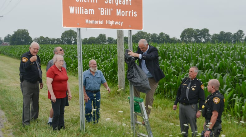 Family members of Sheriff Sgt. William "Bill" Morris, a Miami County sheriff's deputy killed in the line of duty Nov. 22, 1972, near Tipp City, were among those attending an unveiling of a sign designating a section of Ohio 55 just west of Troy in honor of Morris on July 27, 2023. Also at the unveiling were retired Deputy Billy Ray, sheriff's office representatvies and State Sen. Steve Huffman (R-Tipp City), pictured on the ladder just after the unveiling. CONTRIBUTED PHOTO
