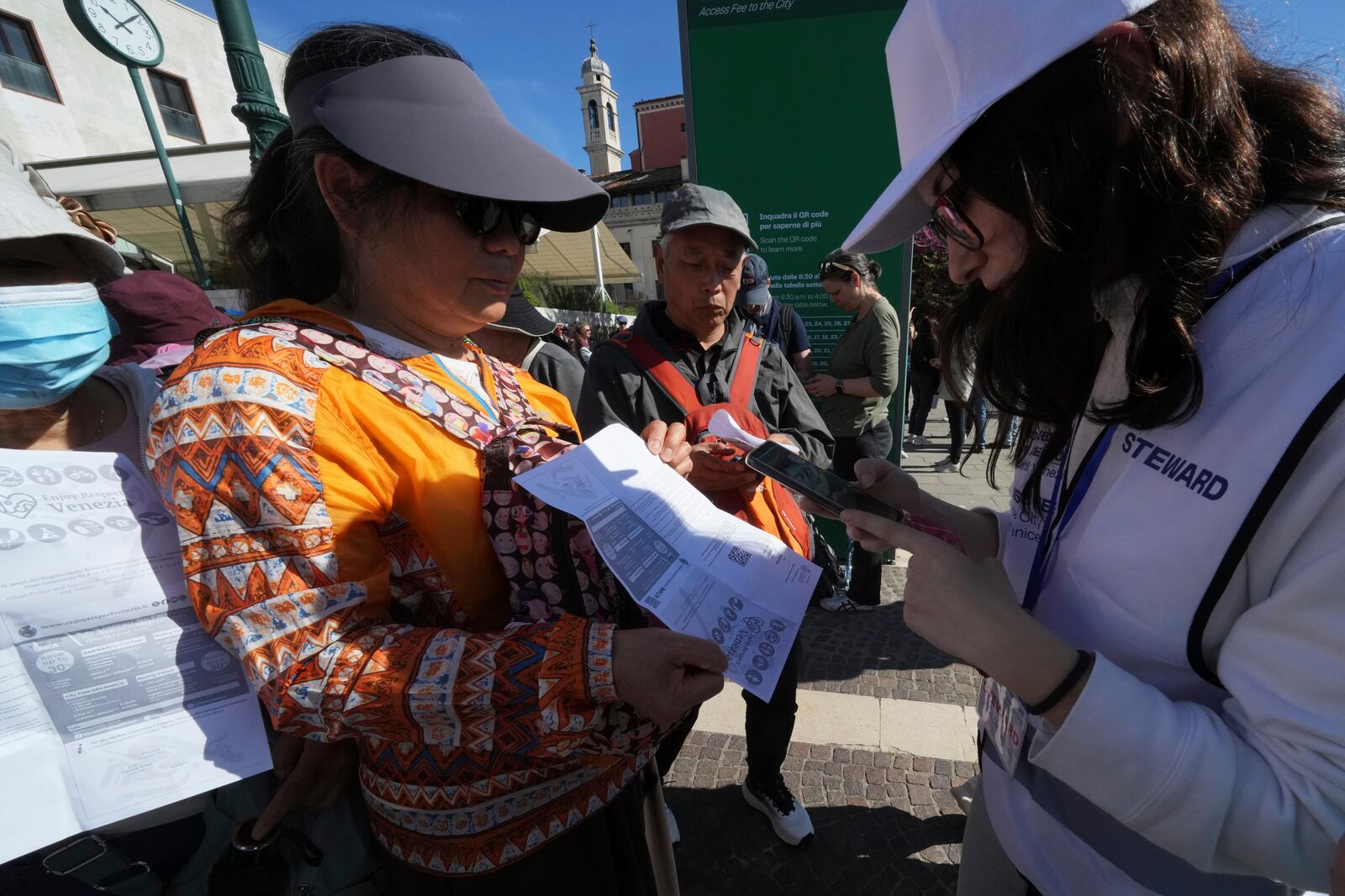 Stewards check tourists' QR codes outside the main train station in Venice, Italy, Friday, April 18, 2025, as the city for a second year is charging day-trippers an arrivals tax. (AP Photo/Antonio Calanni)