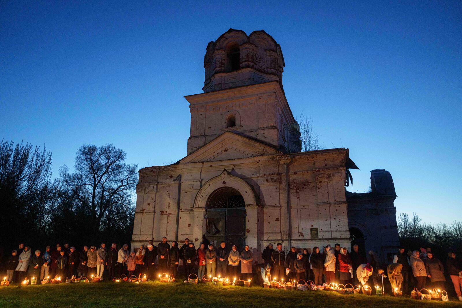 People stand in line to have their Easter baskets blessed in front of a church destroyed in fighting between Russian and Ukrainian forces, during celebration of the Orthodox Easter in Lukashivka village, Ukraine, on Sunday, April 20, 2025. (AP Photo/Evgeniy Maloletka)