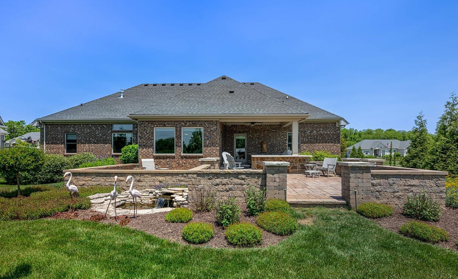 The rear of the home has a stamped concrete patio that is partially covered and has half stone walls surrounding it. There is also a koi pond and two outbuildings.