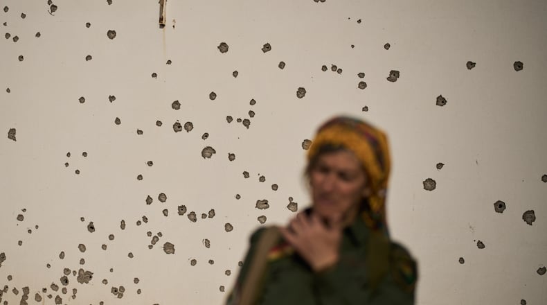 A member of the armed wing of the Kurdish-Iranian opposition group Organization of Iranian Kurdistan Struggle, known as Khabat, stands in front of a shrapnel pockmarked wall that allegedly was damaged in strike by Iranian-backed militias in Iraq last week at a military base on the outskirts of Irbil, Iraq, Monday, March 16, 2026. (AP Photo/Leo Correa)