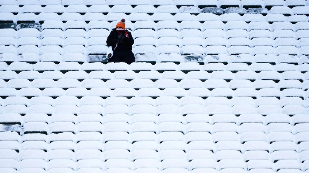 A fan sits in the stadium seats covered in snow before an NFL football game between the Cincinnati Bengals and the Baltimore Ravens, Sunday, Dec. 14, 2025, in Cincinnati. (AP Photo/Carolyn Kaster)