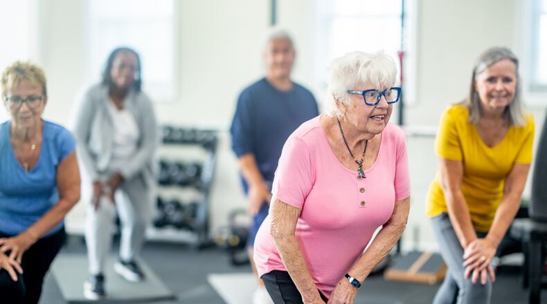 A small group of diverse seniors work out in a small fitness studio together. They are each dressed comfortably as they hold a stretch and focus on their breathing. CREDIT: FATCAMERA/ISTOCK