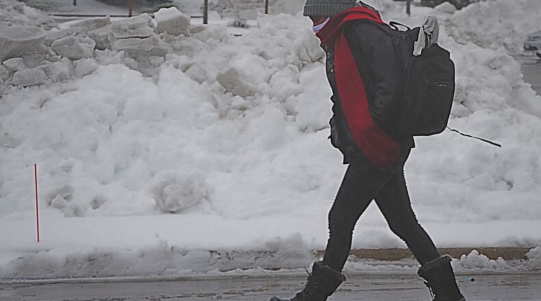 A person walks passed a snow pile of on Crossing Boulevard in Beavercreek Sunday, Jan. 31, 2021. MARSHALL GORBY\STAFF