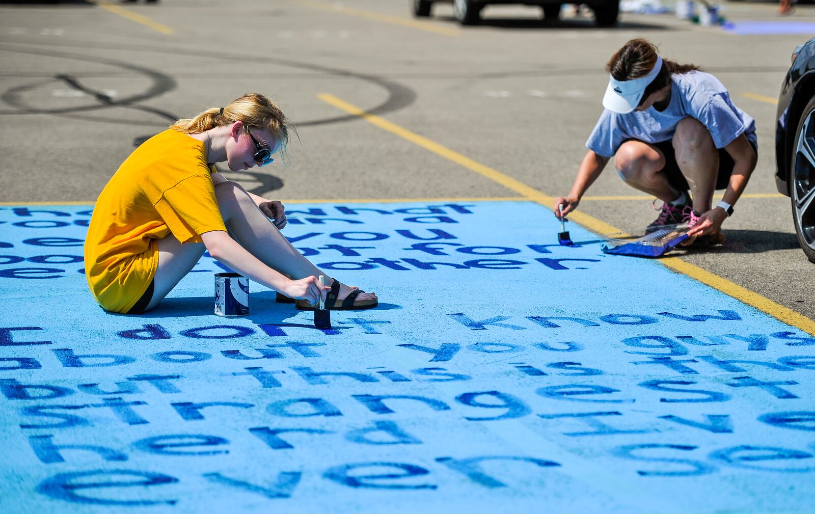 Emma Krabbe, left, a Lakota East senior, paints a design on her parking spot with the help of her mom, Melissa Krabbe, Tuesday, Sept. 4 at Lakota East High School in Liberty Township. The message is a quote from the movie Ice Age. Seniors got the opportunity to personalize their parking spots for the first time. NICK GRAHAM/STAFF