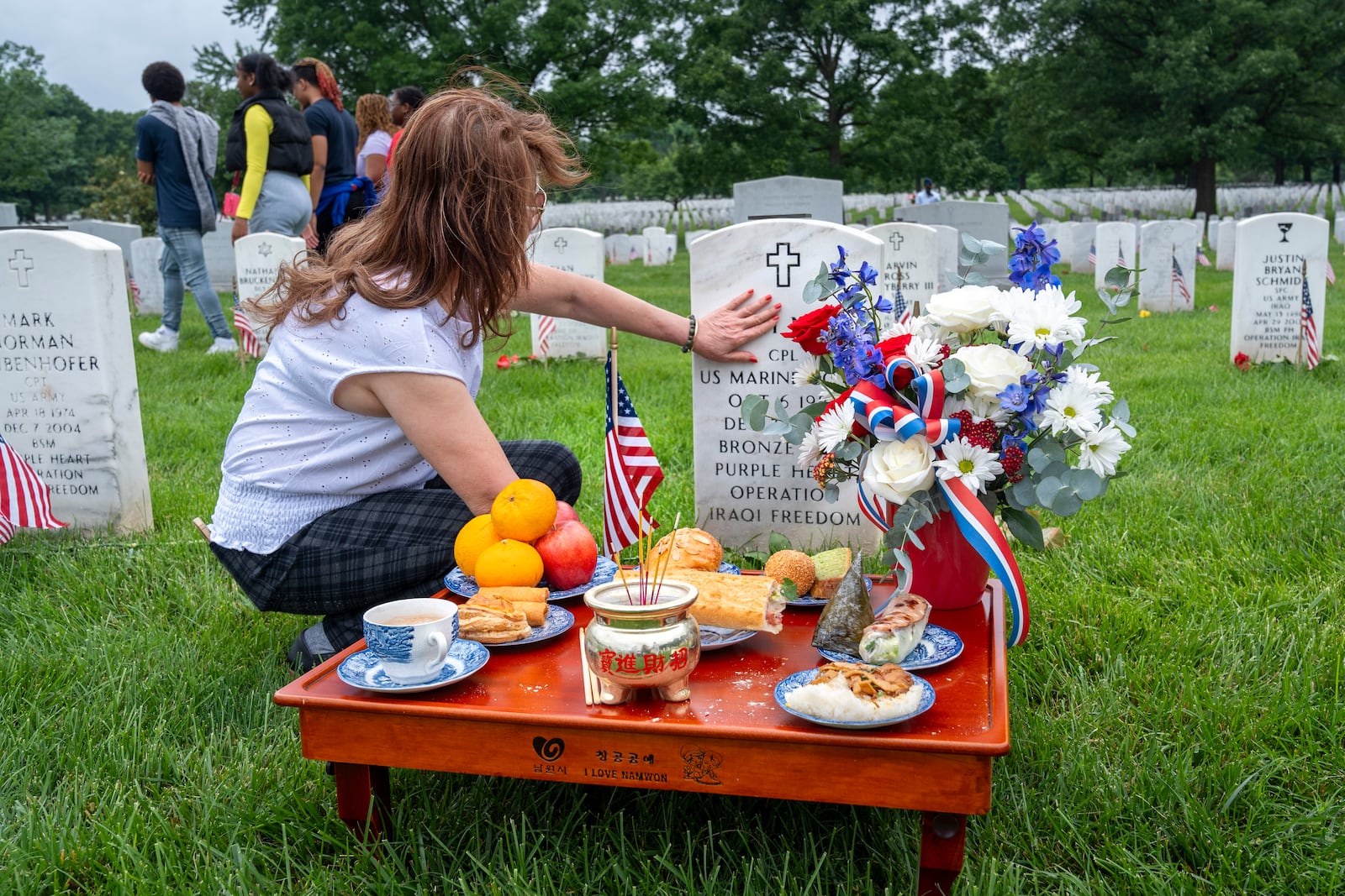 FILE - Kim Hoan Nguyen, of Falls Church, Va., who is originally from Vietnam, touches her son's gravestone next to ritual offerings in the Vietnamese tradition at the gravesite of her son, Marine Corporal Binh N Le, who died serving in Iraq in 2004, in Section 60 of Arlington National Cemetery, in Arlington, Va., Monday, May 27, 2024, on Memorial Day. (AP Photo/Jacquelyn Martin, File)