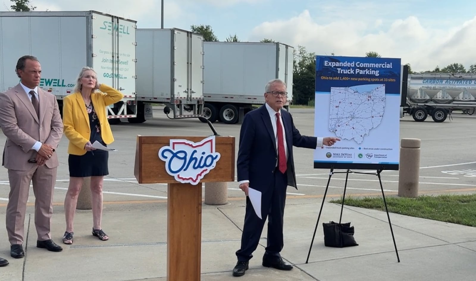 Ohio Gov. Mike DeWine announced a new effort to expand commercial truck parking in the state Tuesday, July 29, 2025, during a press briefing at the southbound Interstate 71 rest stop in Oregonia in Warren County. Plans call for the addition of at least 1,400 new truck parking spaces at 33 state-maintained sites across Ohio, including 100 more at the southbound I-71 rest stop in Warren County. Pictured to left are Tom Balzer, president and CEO of the Ohio Trucking Association, and Pamela Boratyn, Ohio Department of Transportation director. JEN BALDUF/STAFF