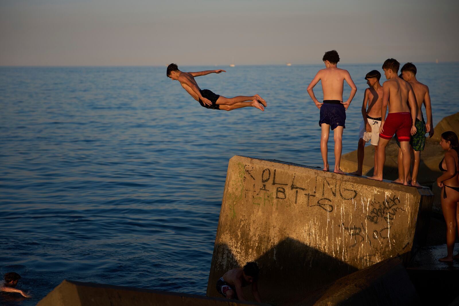 Young swimmers jump into the water from a rock on a breakwater on a hot day in Barcelona, Spain, Sunday, June 29, 2025. (AP Photo/Emilio Morenatti)
