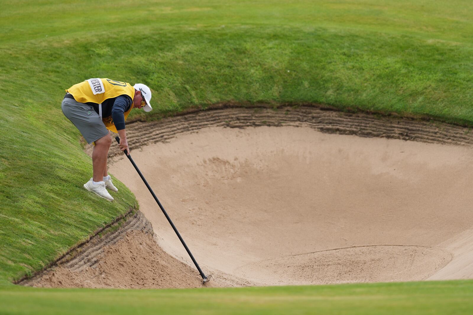 Jason Reynolds caddie for Dean Burmester of South Africa of South Africa, rakes a bunker on the 1st after Burmester played a shot from it during the third round of the British Open golf championship at the Royal Portrush Golf Club, Northern Ireland, Saturday, July 19, 2025. (AP Photo/Jon Super)