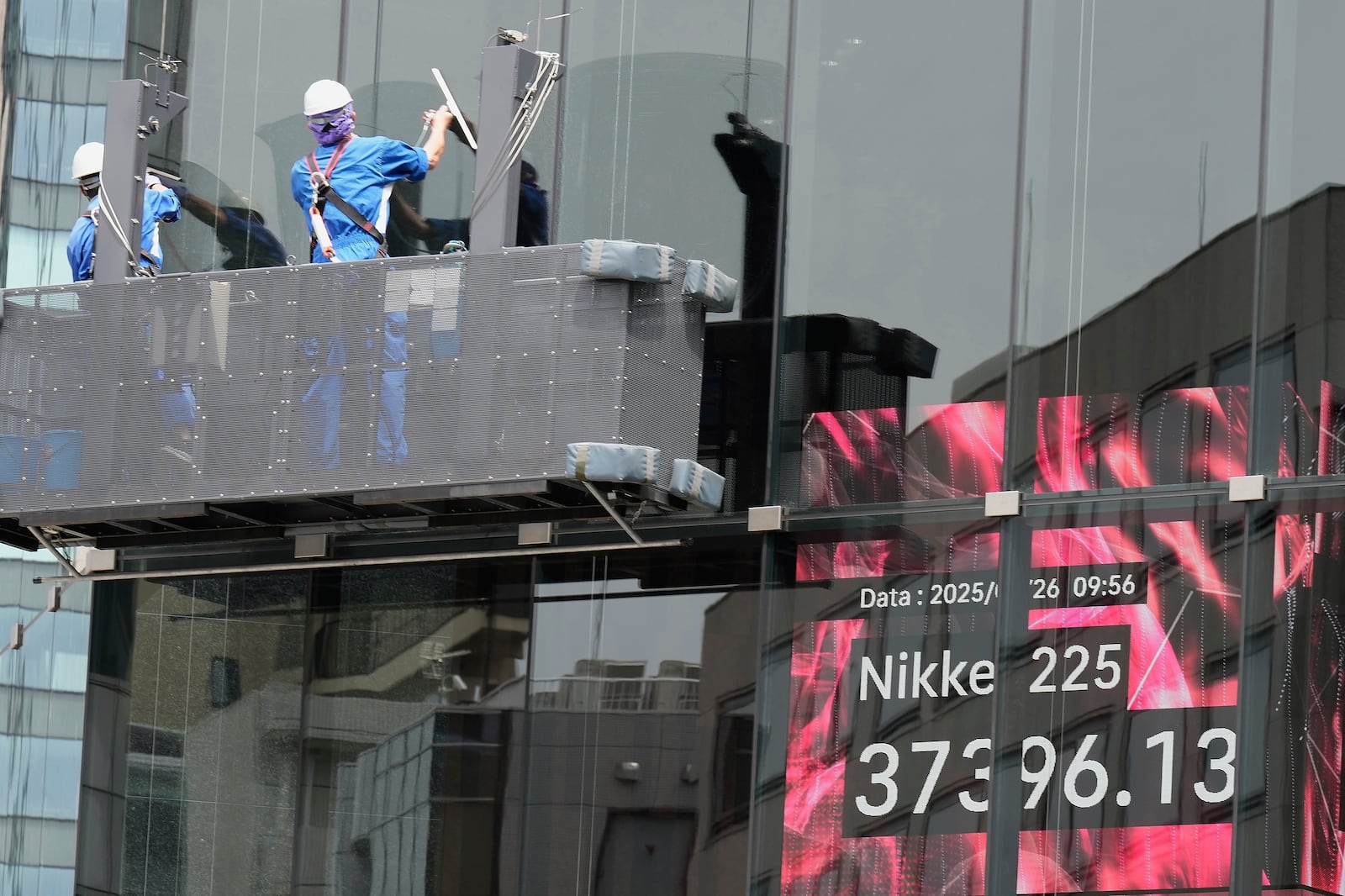 Workers clean the glass window of a building in front of an electronic stock board showing Japan's Nikkei index at a securities firm Monday, May 26, 2025, in Tokyo. (AP Photo/Eugene Hoshiko)