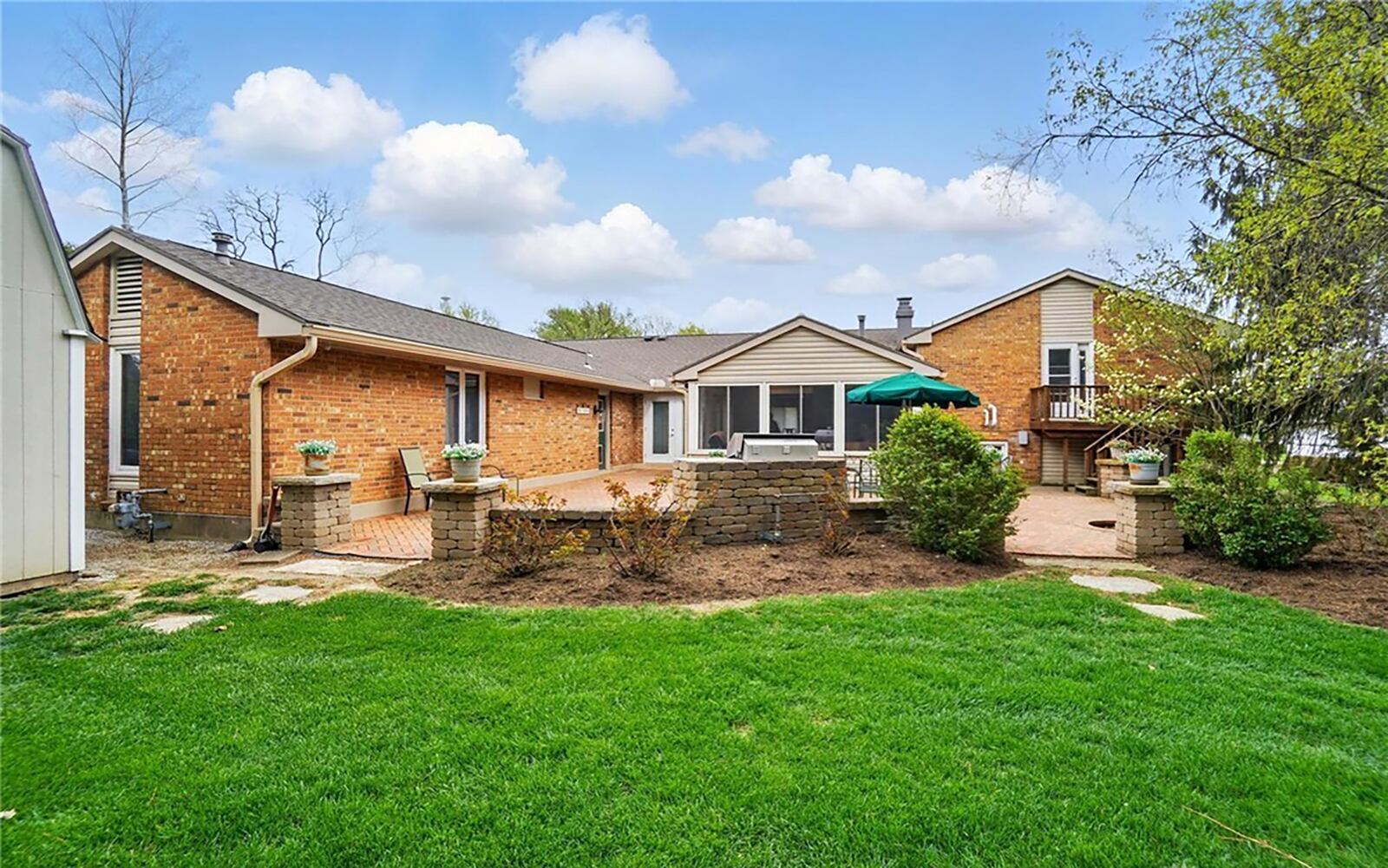 The rear of the home features a brick paver patio and raised wood deck off the primary bedroom suite