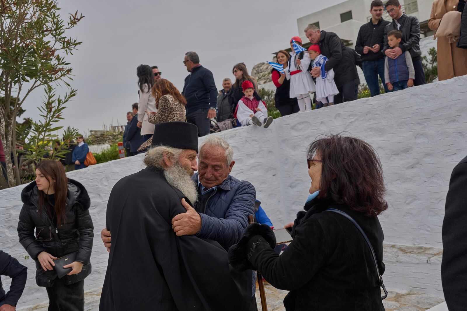 Orthodox Christian monk Father Spyridon is hugged by islanders as people gather to watch a parade for Greek Independence Day, which commemorates the start of the Greek War of Independence in 1821, in Amorgos island, Greece, on Tuesday, March 25, 2025. (AP Photo/Petros Giannakouris)